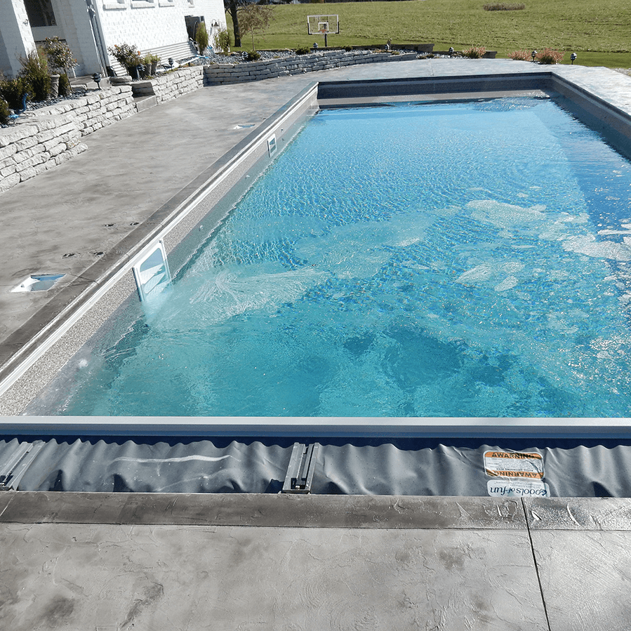 A large swimming pool surrounded by concrete with a basketball hoop in the background