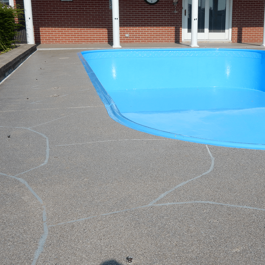 A blue swimming pool surrounded by decorative concrete with a brick house in the background