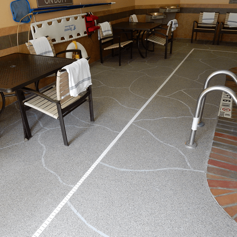 A room with tables and chairs on a decorative concrete floor next to a swimming pool