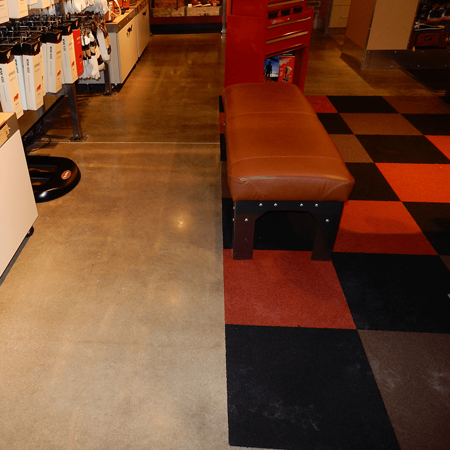 A checkered rug with a brown bench in the middle on a shiny concrete floor