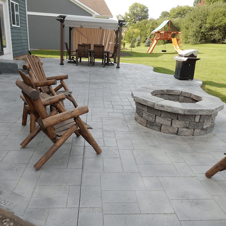 A decorative concrete patio with chairs and a fire pit in the middle