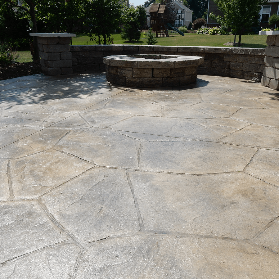 A decorative concrete patio with a fire pit in the middle