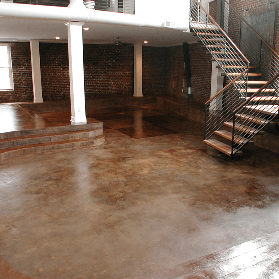 An empty room with a staircase, brick walls, and a shiny concrete floor