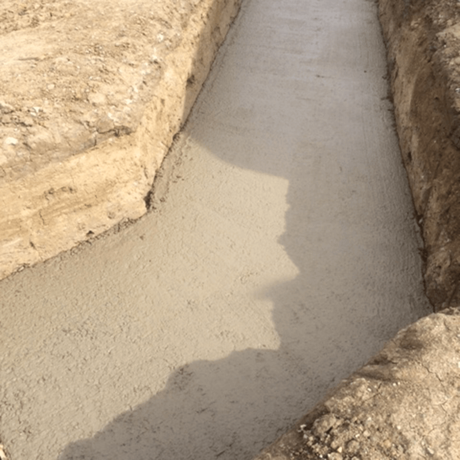 A shadow of a person is cast on the ground in a concrete trench.