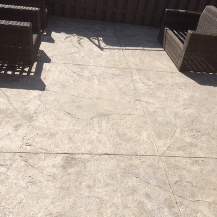 A decorative concrete patio with wicker chairs and a fence in the background