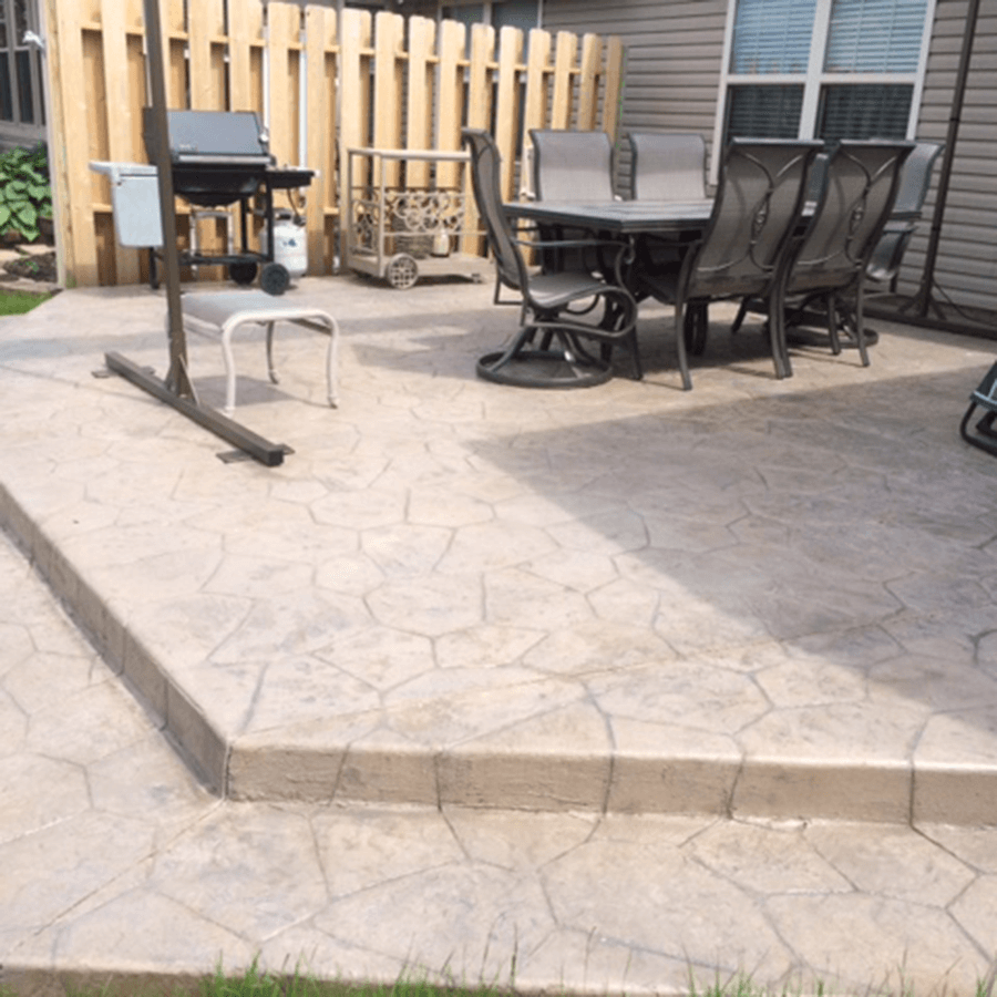 A decorative concrete patio with a table and chairs and a grill