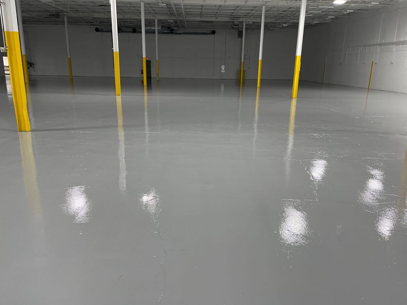A large empty warehouse with a gray floor and yellow poles.