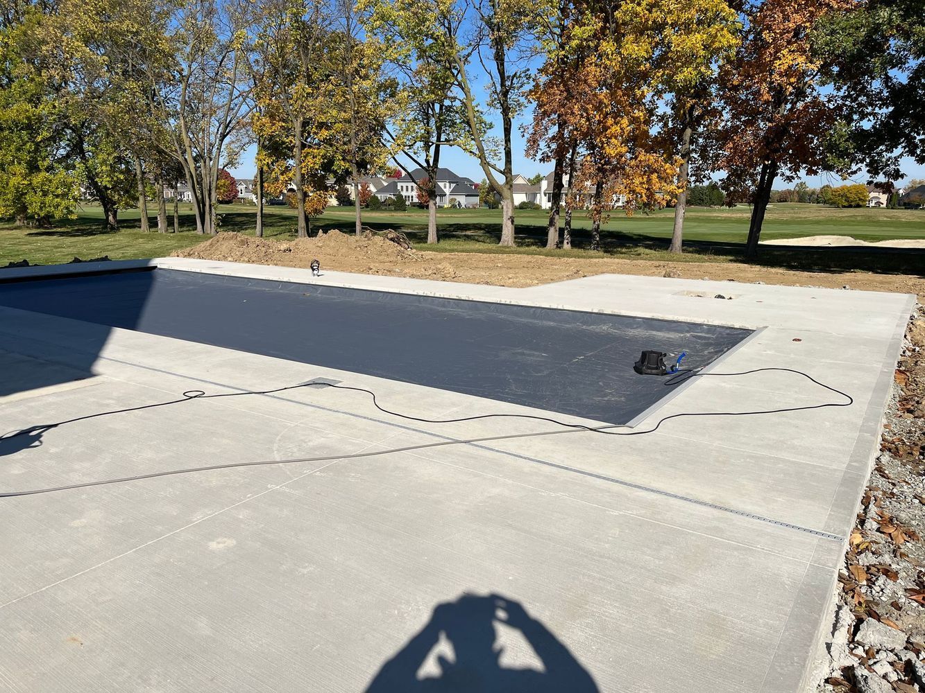 A shadow of a person is cast on a concrete walkway next to a swimming pool.