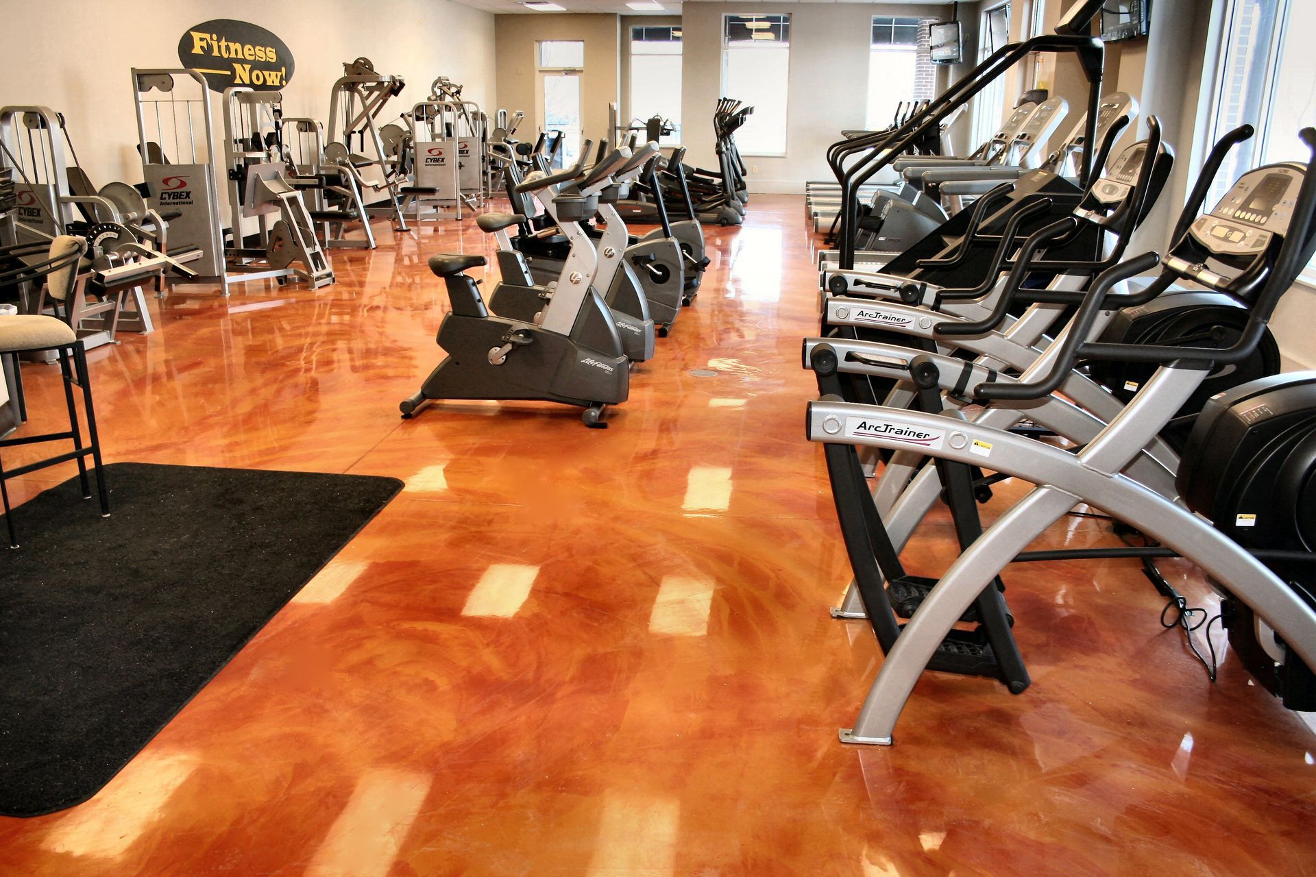 A row of exercise bikes are lined up in a gym on a shiny concrete floor