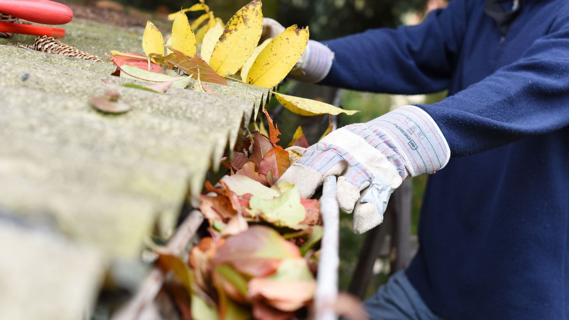 A man is cleaning a gutter with leaves and a hose.