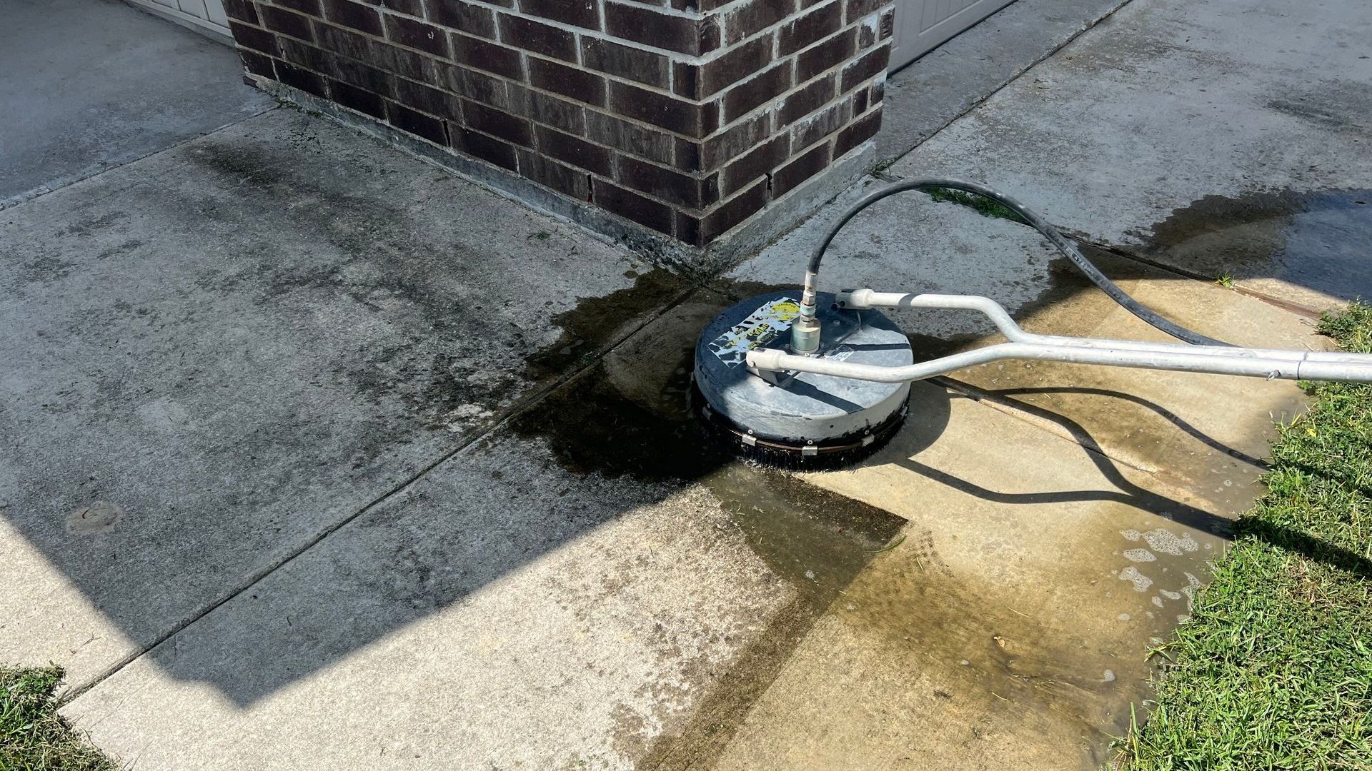 A pressure washer is being used to clean a sidewalk in front of a brick building.