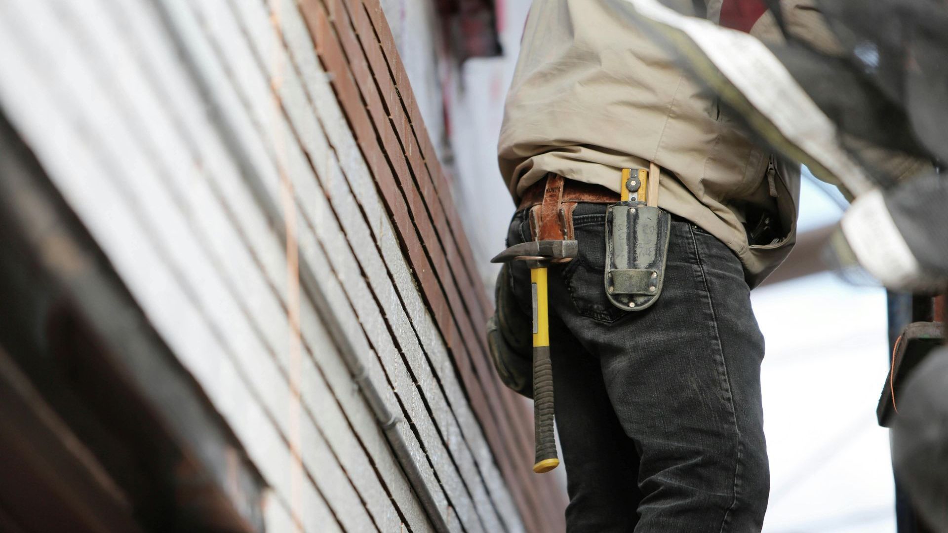 A man is carrying a hammer and a measuring tape in his belt.