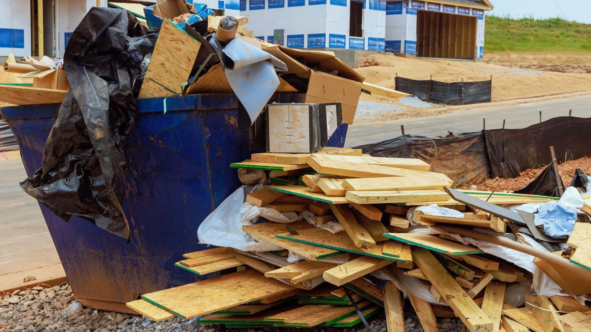 A pile of wood is sitting next to a dumpster at a construction site.