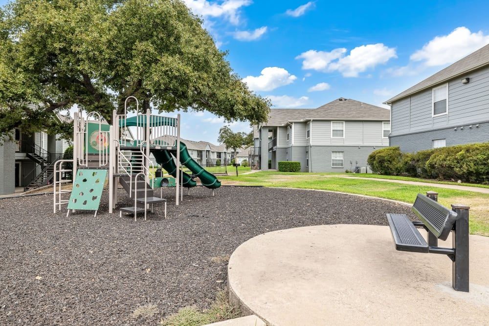 a playground with a slide and a bench in front of a building at The Park at Flower Mound in Flower Mound, TX.
