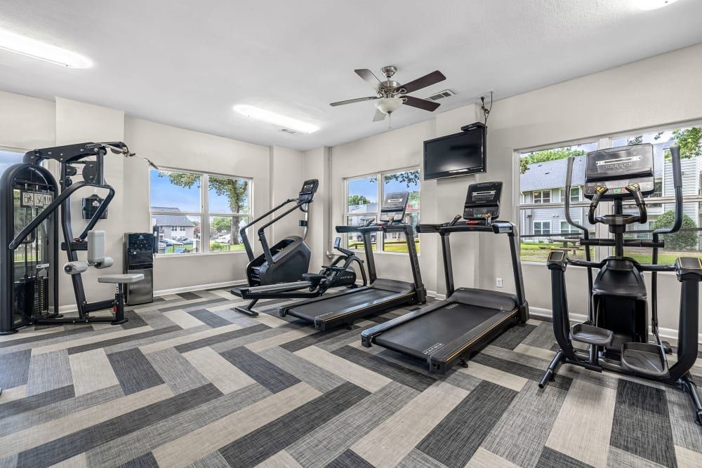 a gym with treadmills , exercise bikes , and a ceiling fan at The Park at Flower Mound in Flower Mound, TX.