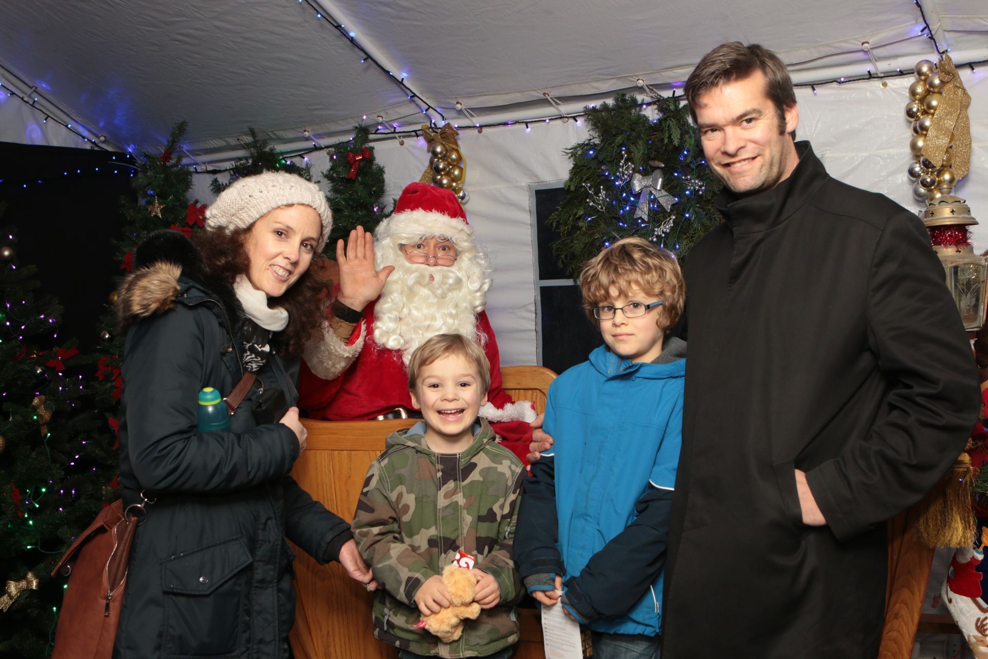 A festive scene inside Santa's grotto, with colourful decorations, twinkling lights, and Santa Claus seated in his chair surrounded by eager children.