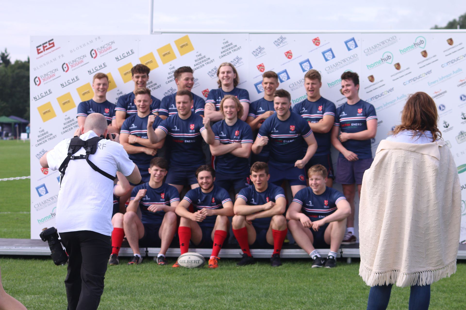 a rugby team being photographed against a logo board or branding board
