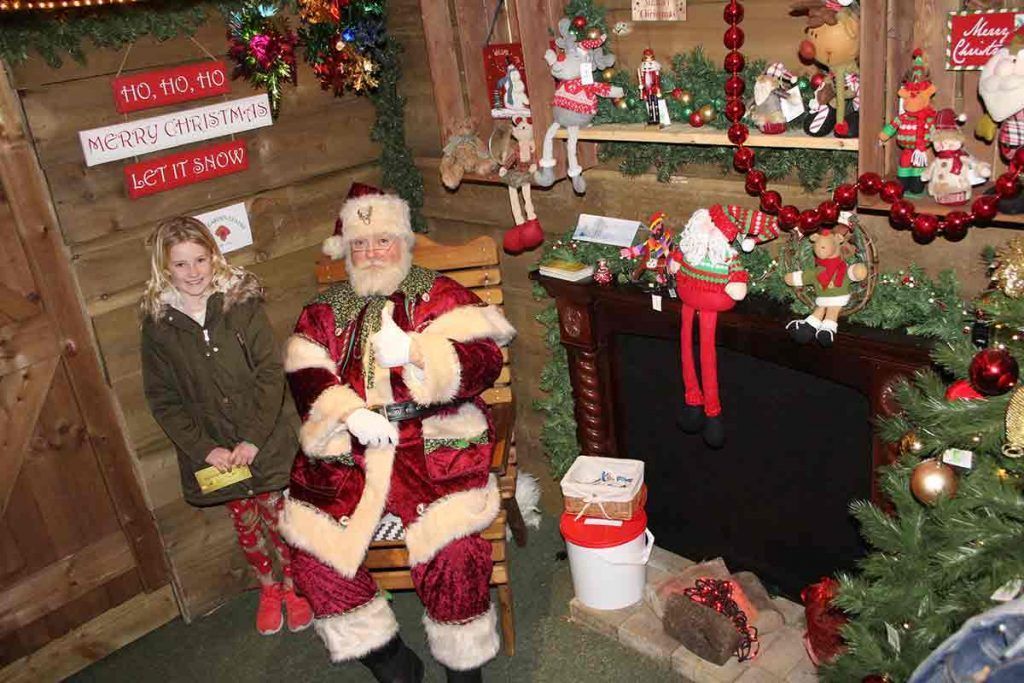 A festive scene inside Santa's grotto, with colourful decorations, twinkling lights, and Santa Claus seated in his chair surrounded by eager children.