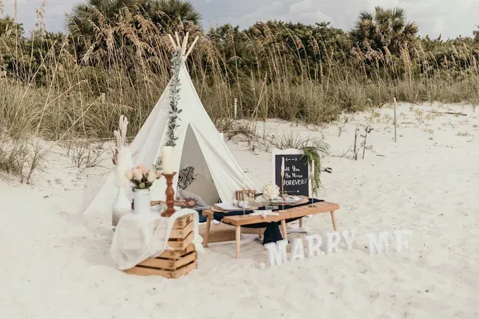 A table setting on a beach with white flowers, candles, and ocean waves in the background.