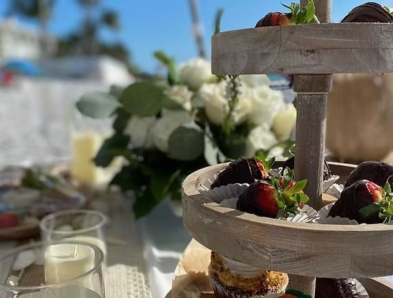 Tiered dessert stand with chocolate-covered strawberries, white flowers, and beach setting.