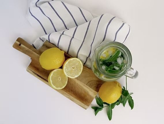 Lemons, mint, and lemonade in a pitcher on a wooden board with a striped towel.