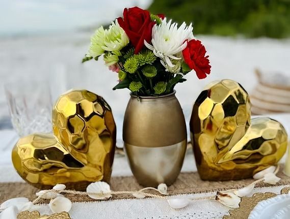 Gold heart decorations flank a vase of red and white flowers on a table.