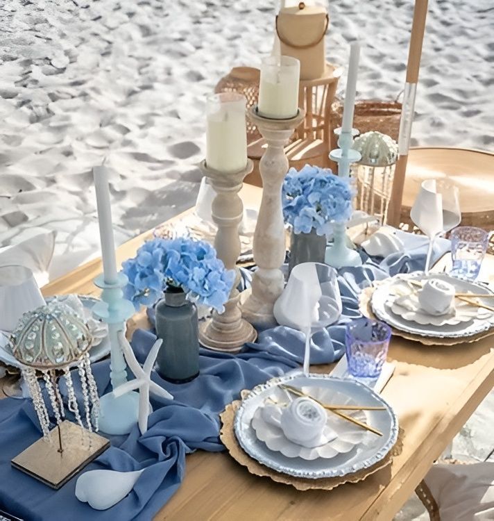 Beach picnic table with blue decor, candles, hydrangeas, and place settings.