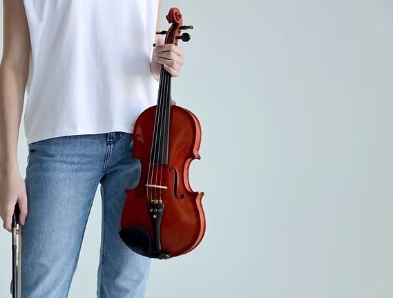 Person in jeans and white shirt holding a violin with bow.