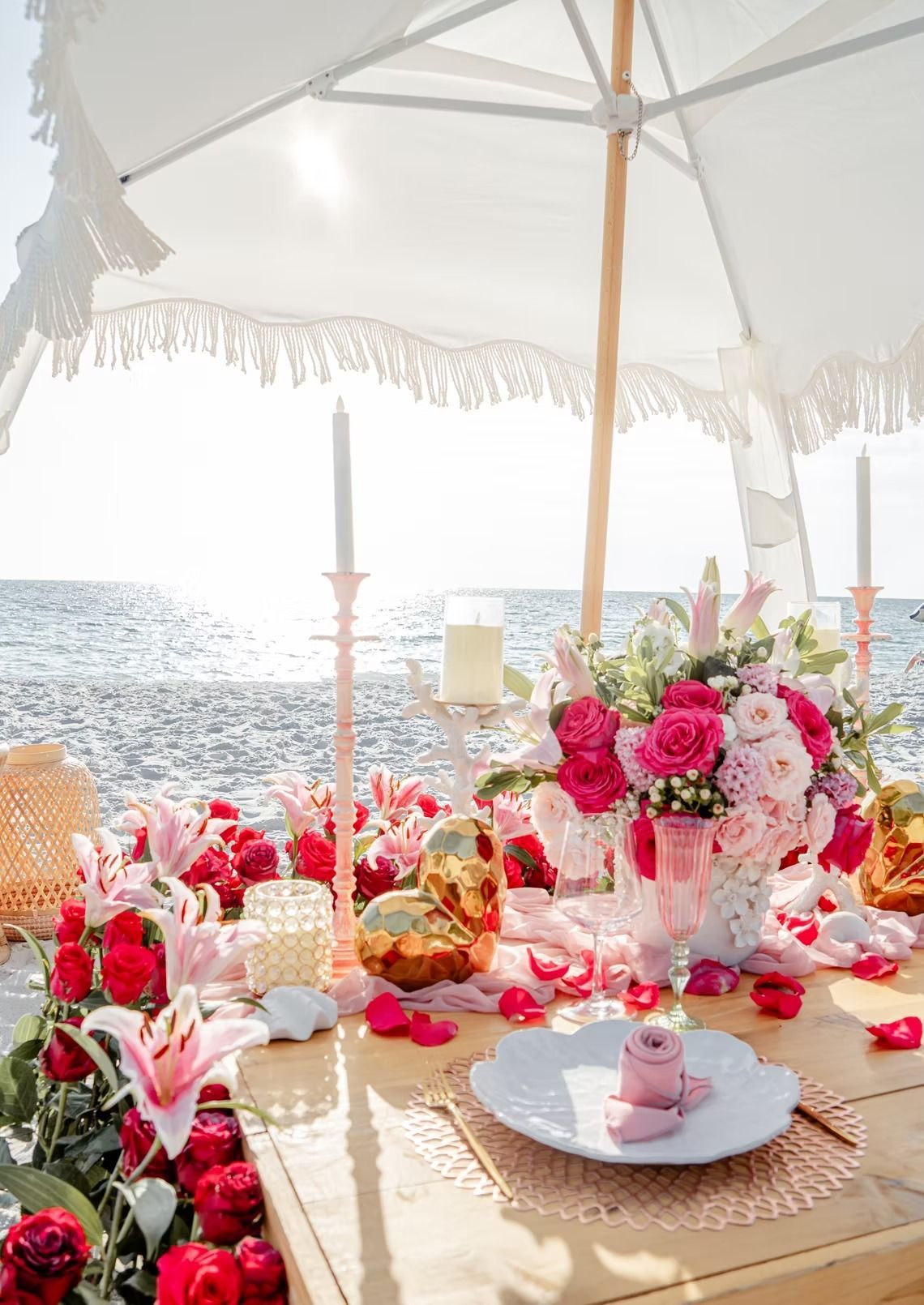 Romantic beach picnic setup with flowers, candles, and ocean backdrop.