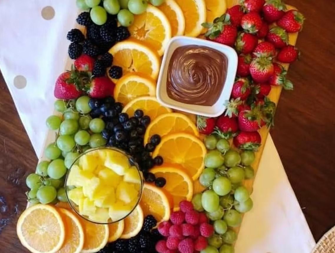 Fruit platter with grapes, berries, oranges, and pineapple, with a dish of chocolate dip.