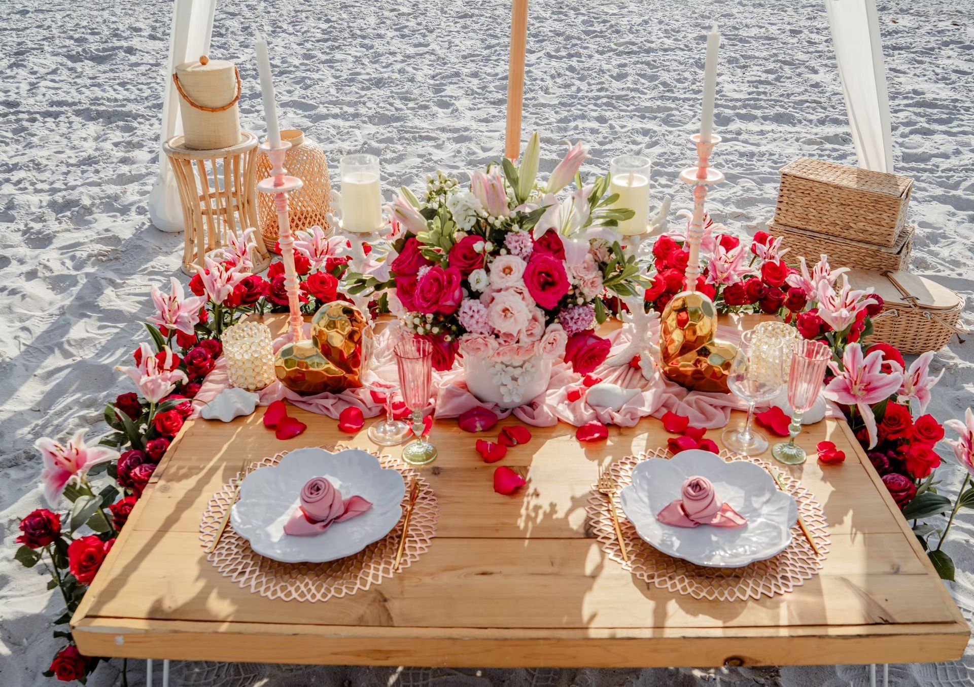 Romantic beach picnic setup with flowers, table, and plates.