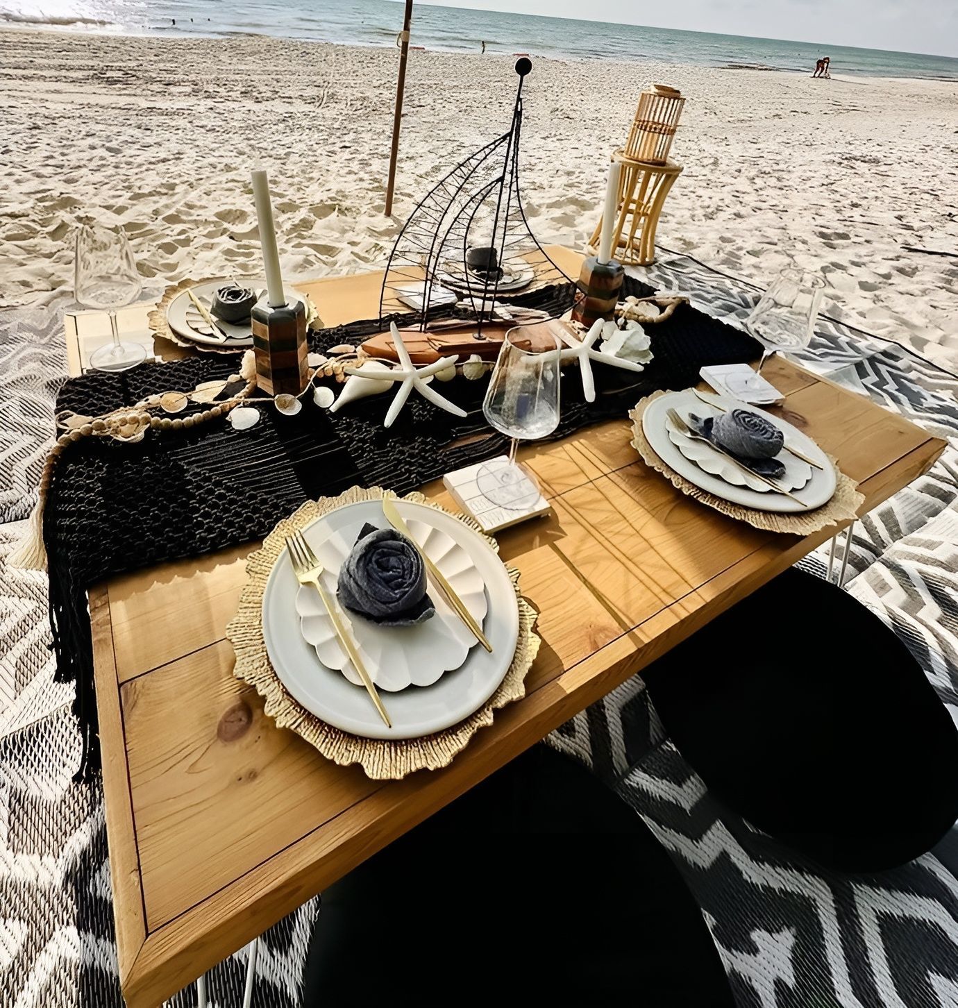 Beach picnic setup with nautical decor on a wooden table, featuring plates, starfish, and seating.