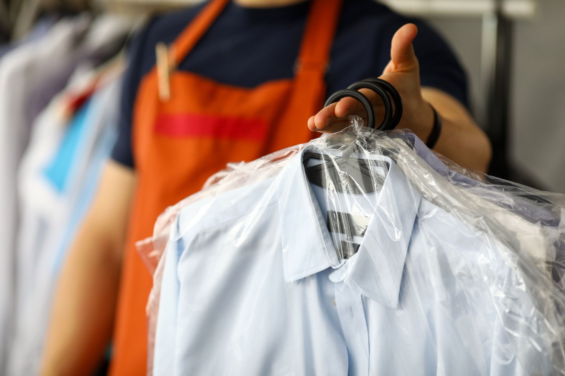 Person in orange apron holding a shirt in plastic wrap.