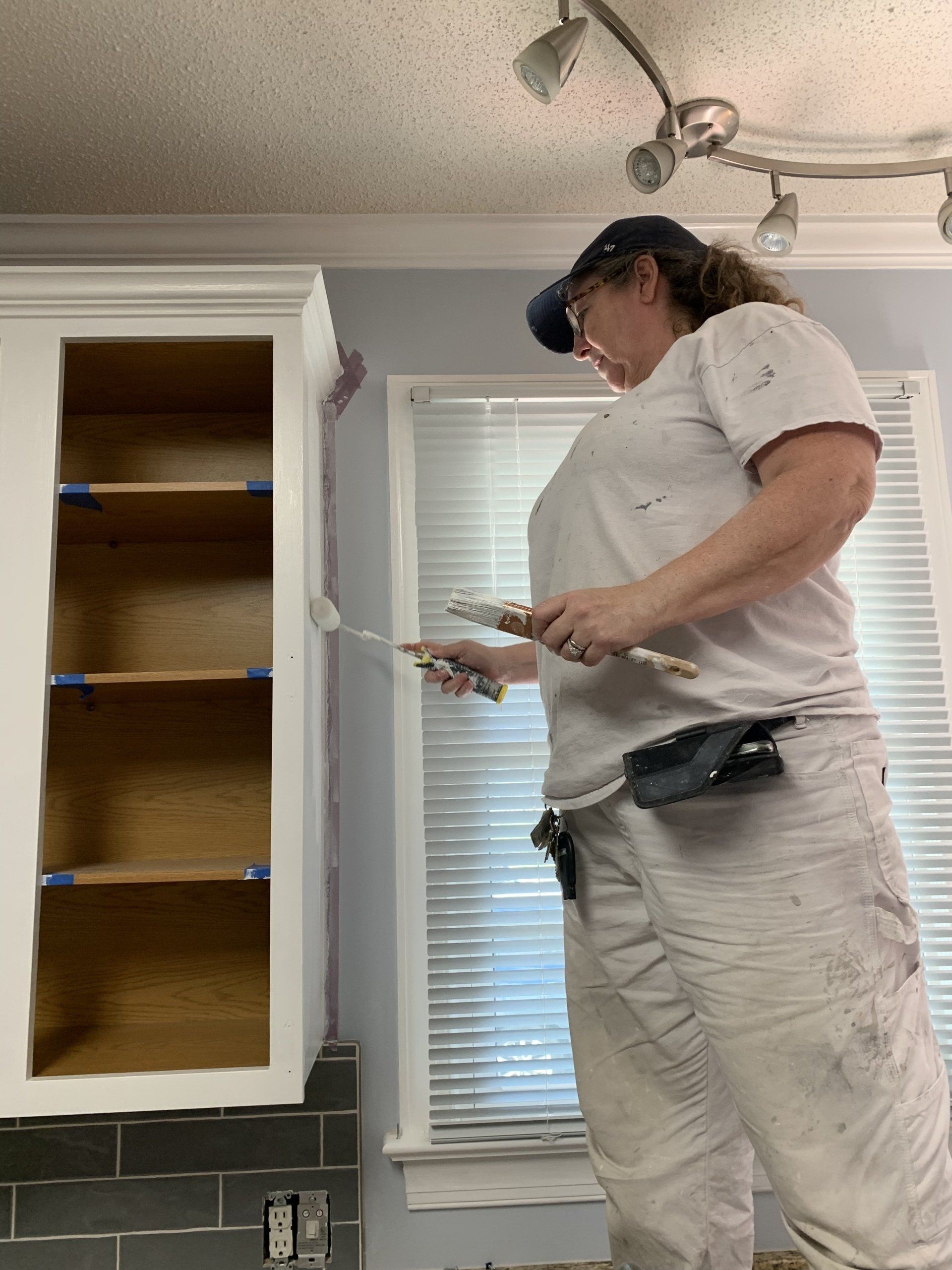 A woman is painting a cabinet in a kitchen.