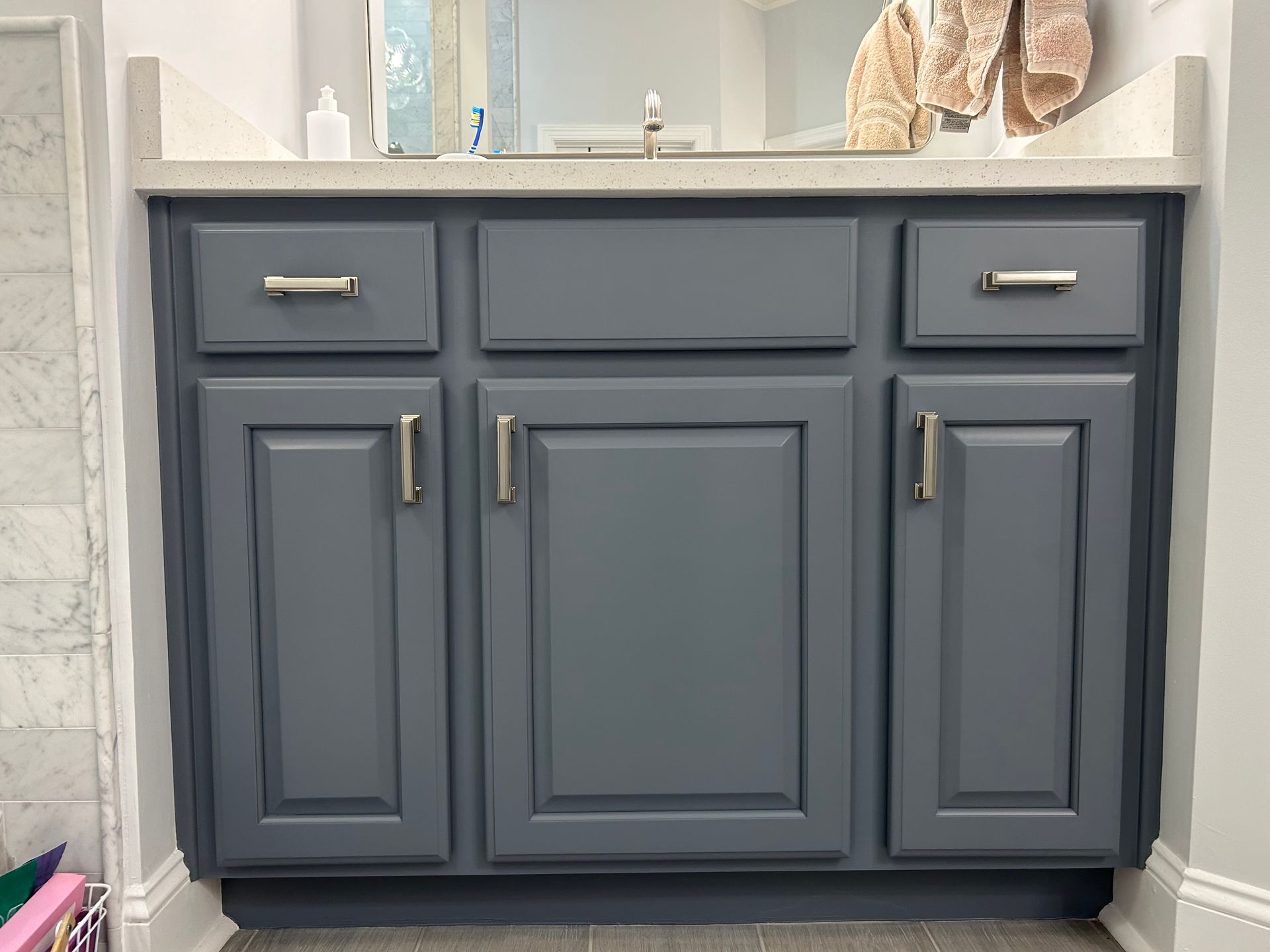 A bathroom vanity with gray cabinets and drawers and a mirror.