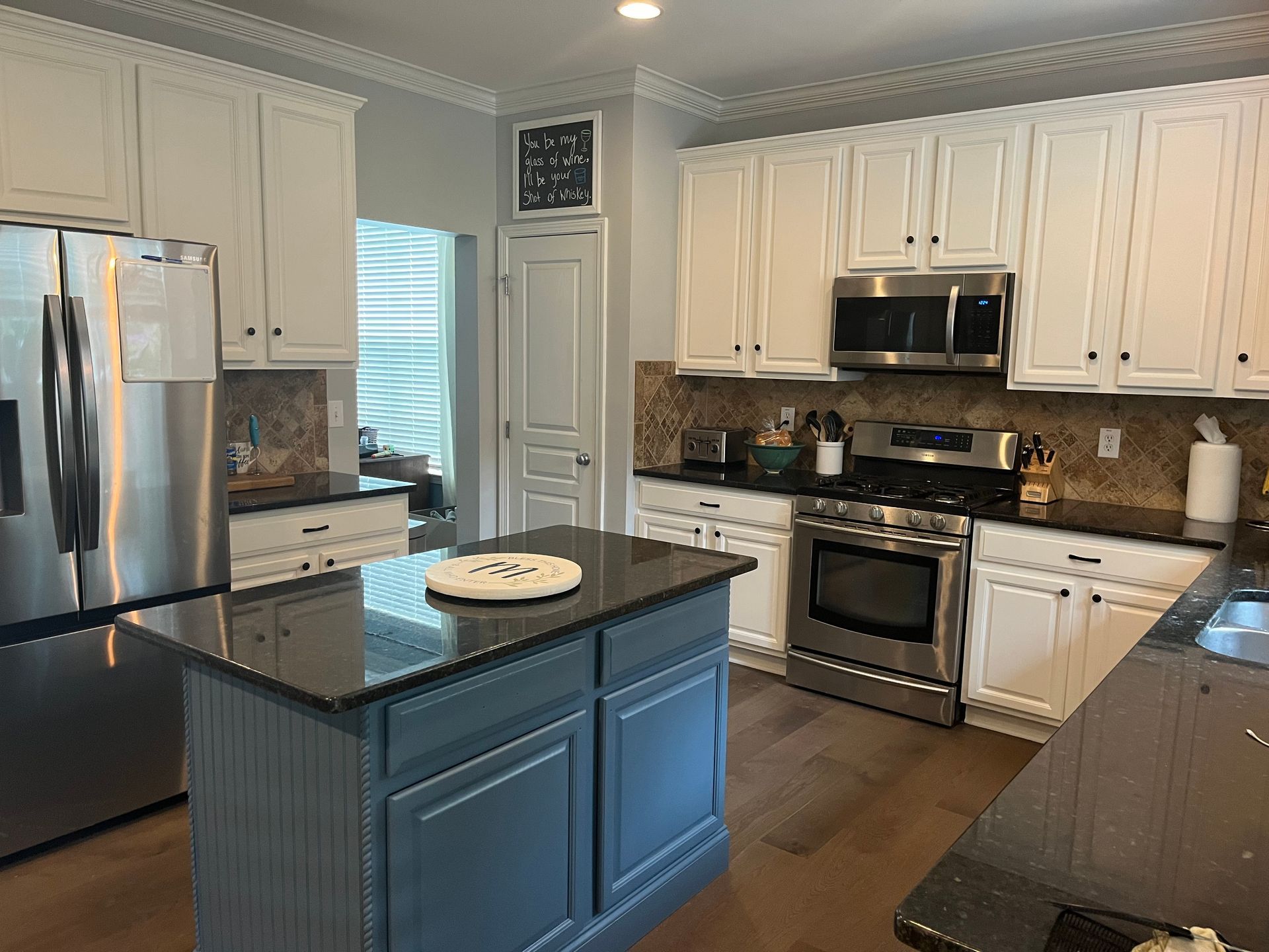 A kitchen with white cabinets , black counter tops , stainless steel appliances and a large island.