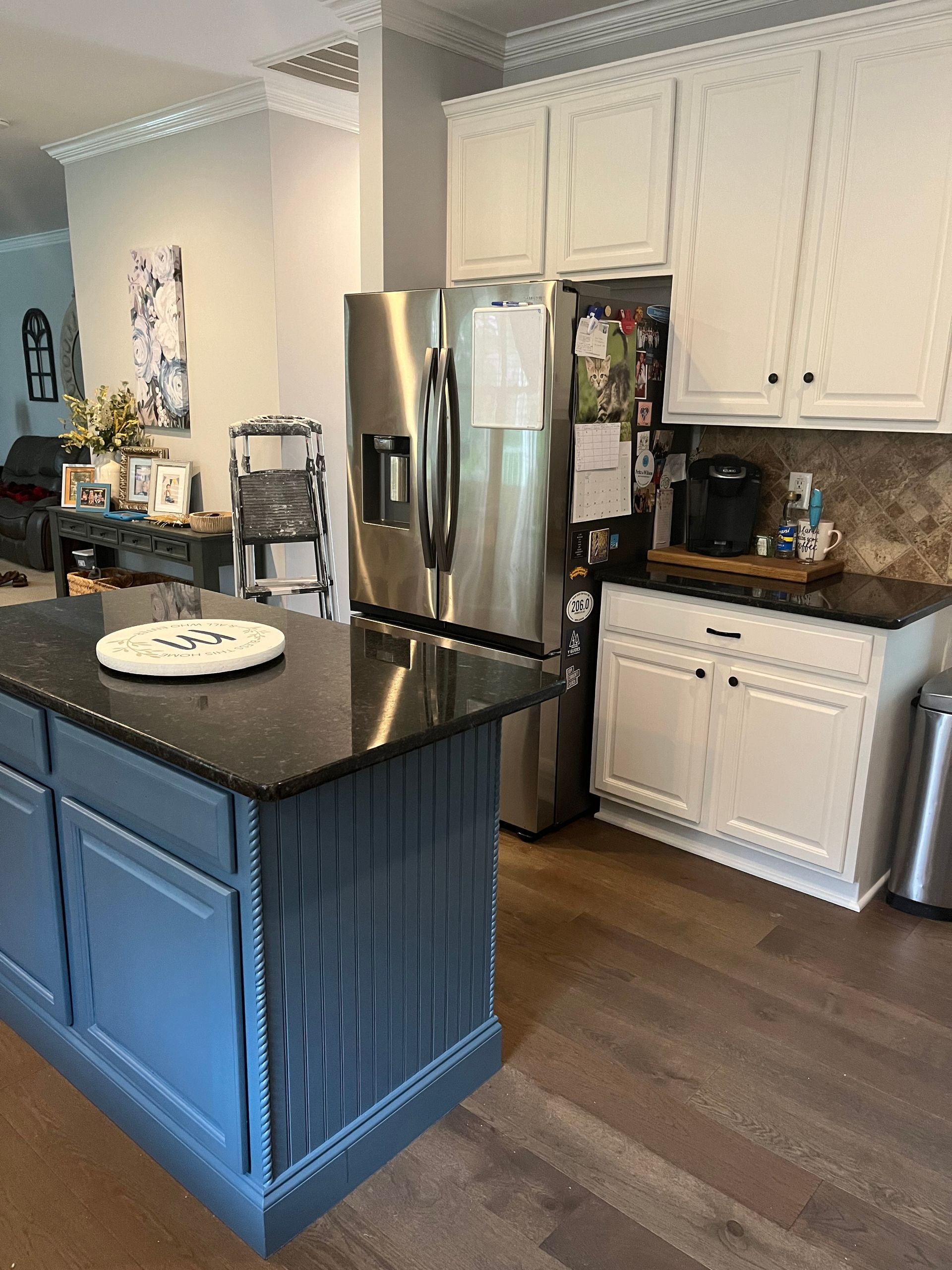 A kitchen with a large island , stainless steel refrigerator , and white cabinets.