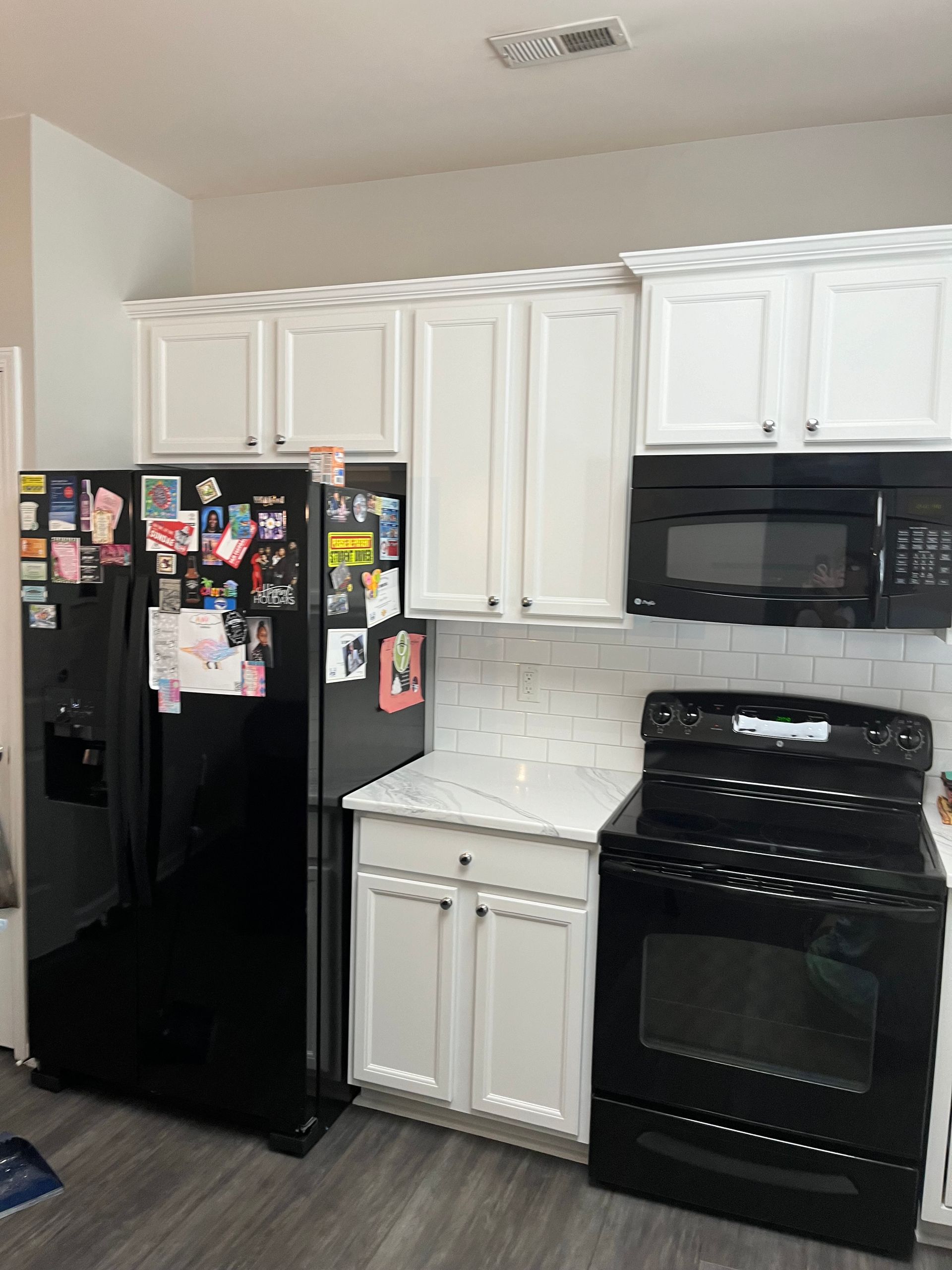 A kitchen with white cabinets , a black refrigerator , a black stove , and a black microwave.