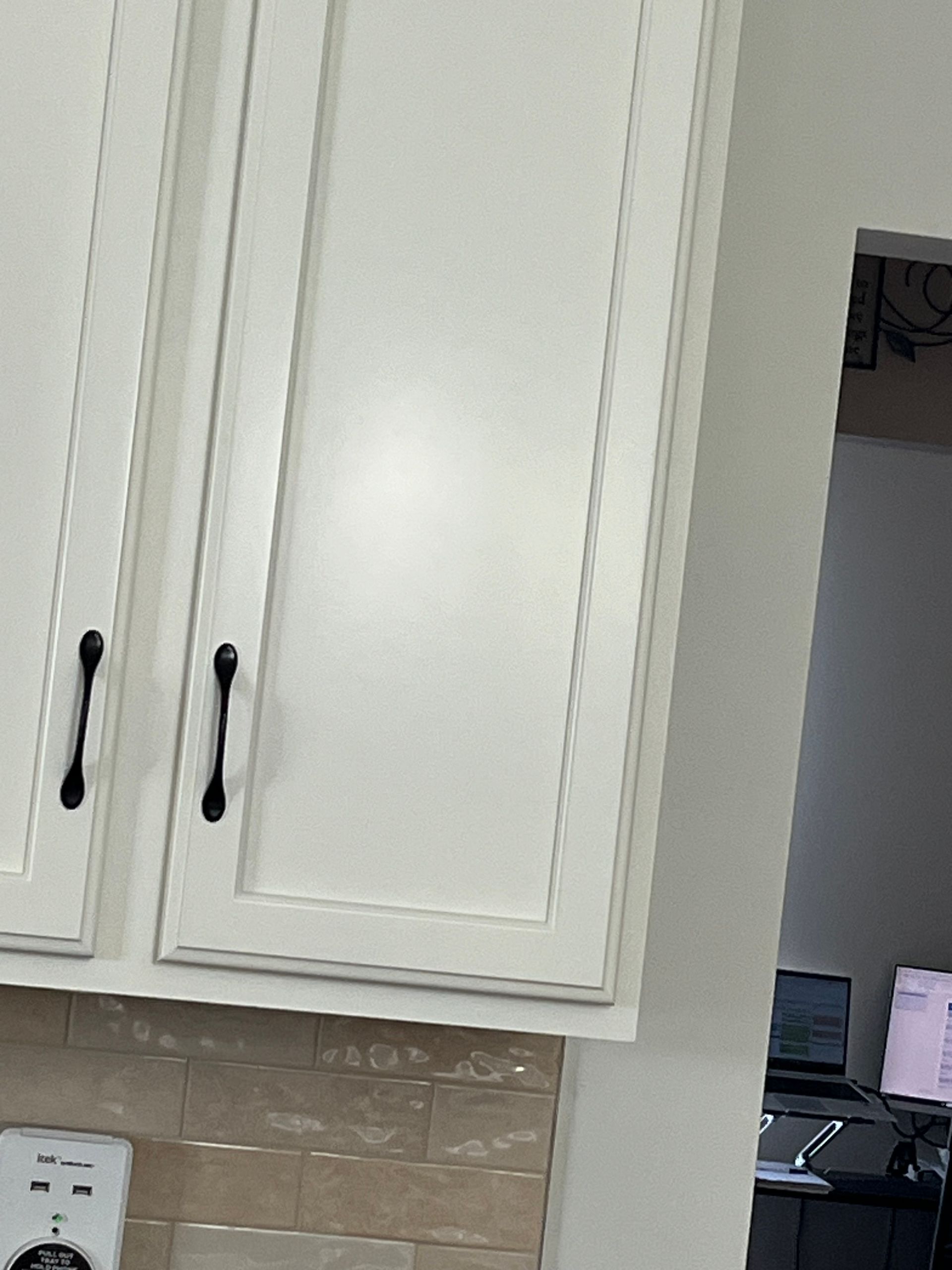 A kitchen with white cabinets and black handles.