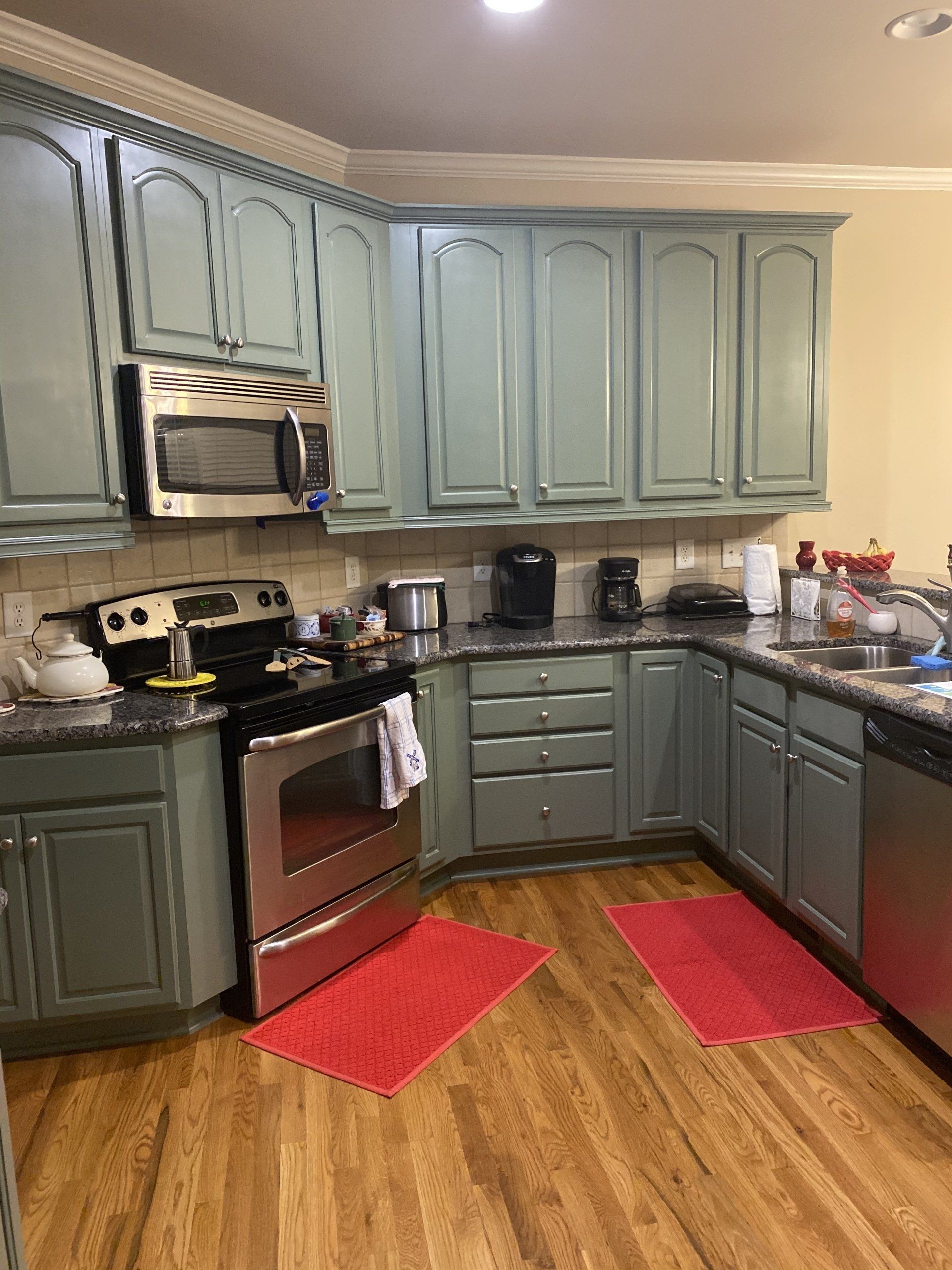 A kitchen with blue cabinets , a stove , a microwave , a sink , and a red rug.