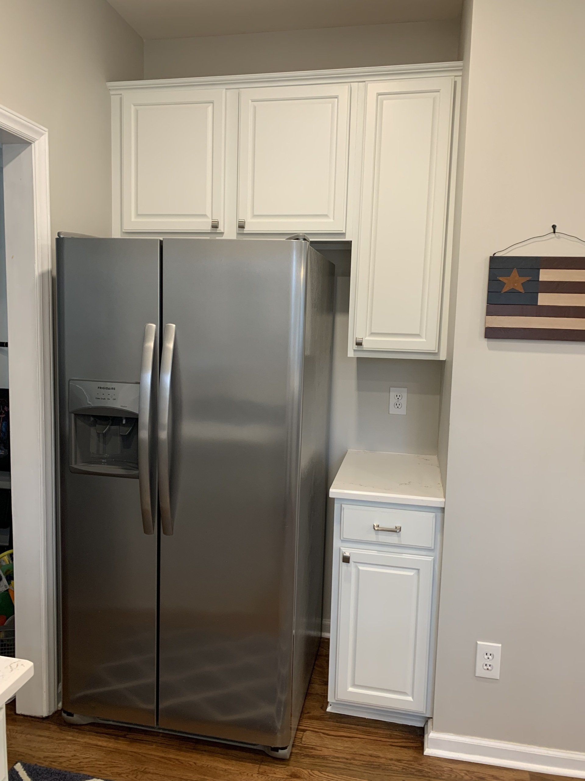 A stainless steel refrigerator is sitting in a kitchen next to white cabinets.