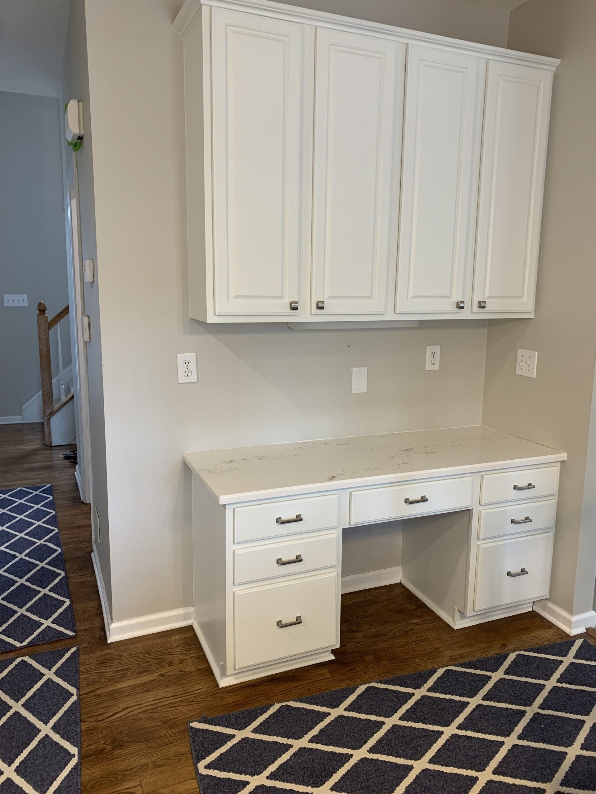 A white desk with drawers and cabinets in a room with a rug.