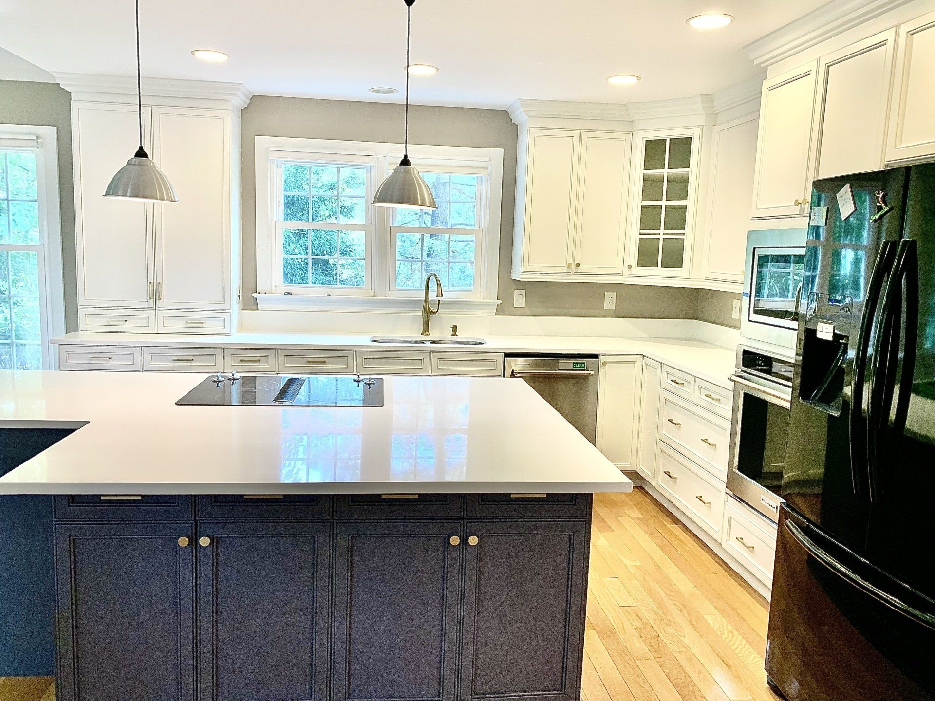 A kitchen with white cabinets , black appliances , a large island , and a black refrigerator.