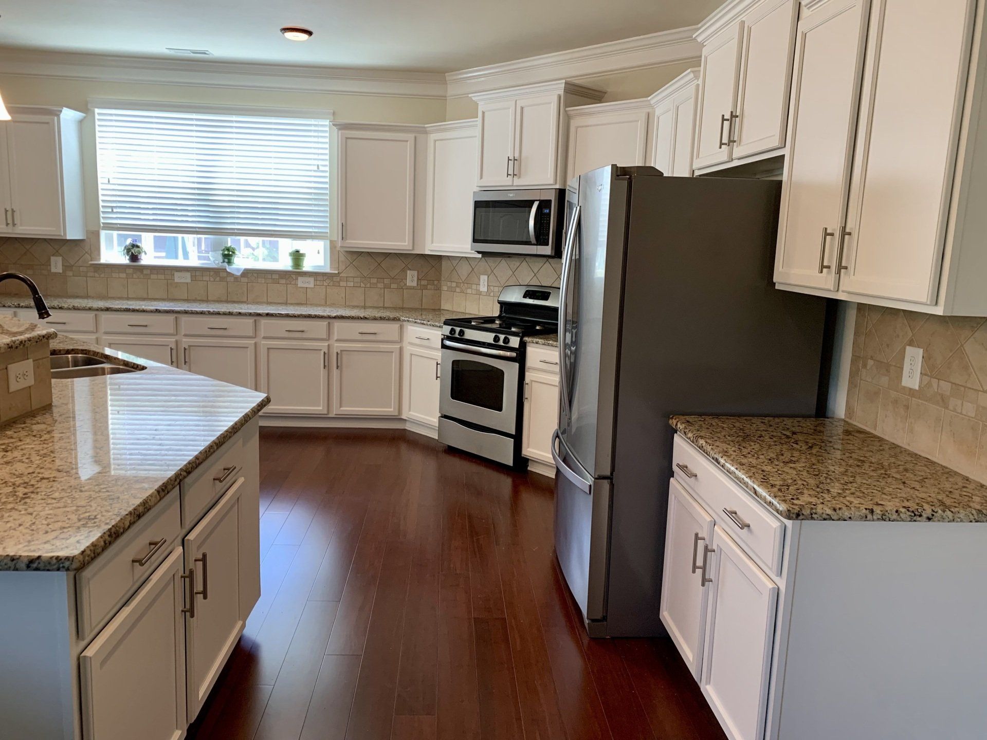 A kitchen with white cabinets , granite counter tops , stainless steel appliances and a refrigerator.