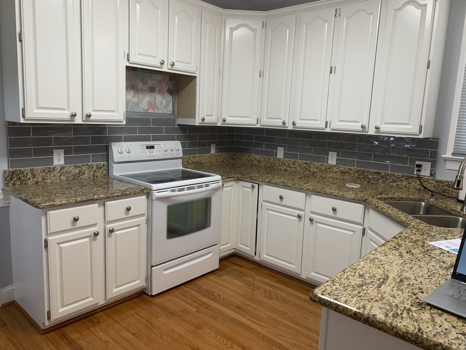 A kitchen with white cabinets , granite counter tops , a stove and a sink.