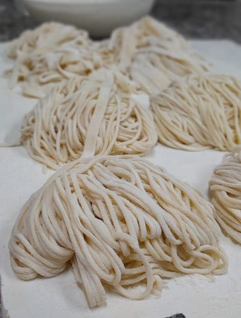 Fideos recién hechos, de color amarillo pálido, dispuestos en nidos sobre una superficie blanca, posiblemente secándose.