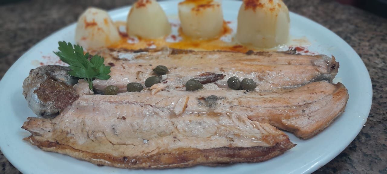 Cocina al aire libre con luces de cadena, una mesa y sillas junto a una ventana.