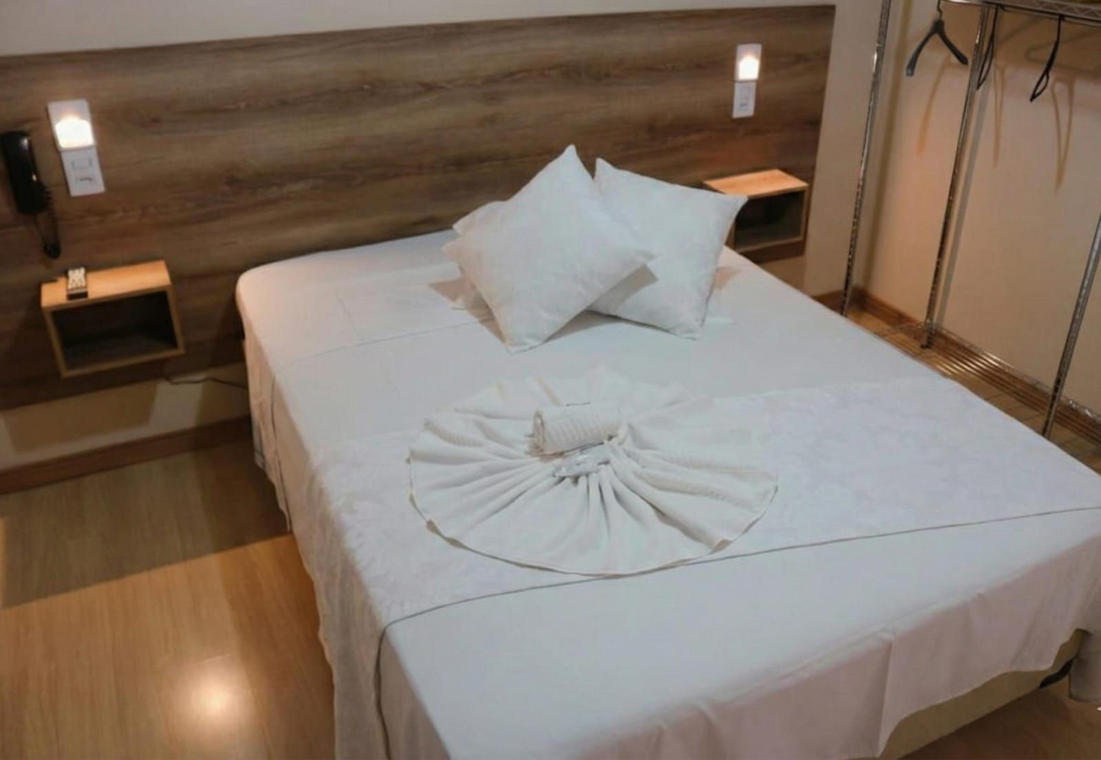 Quarto de hotel com cama equipada com lençóis brancos, travesseiros e toalha dobrada