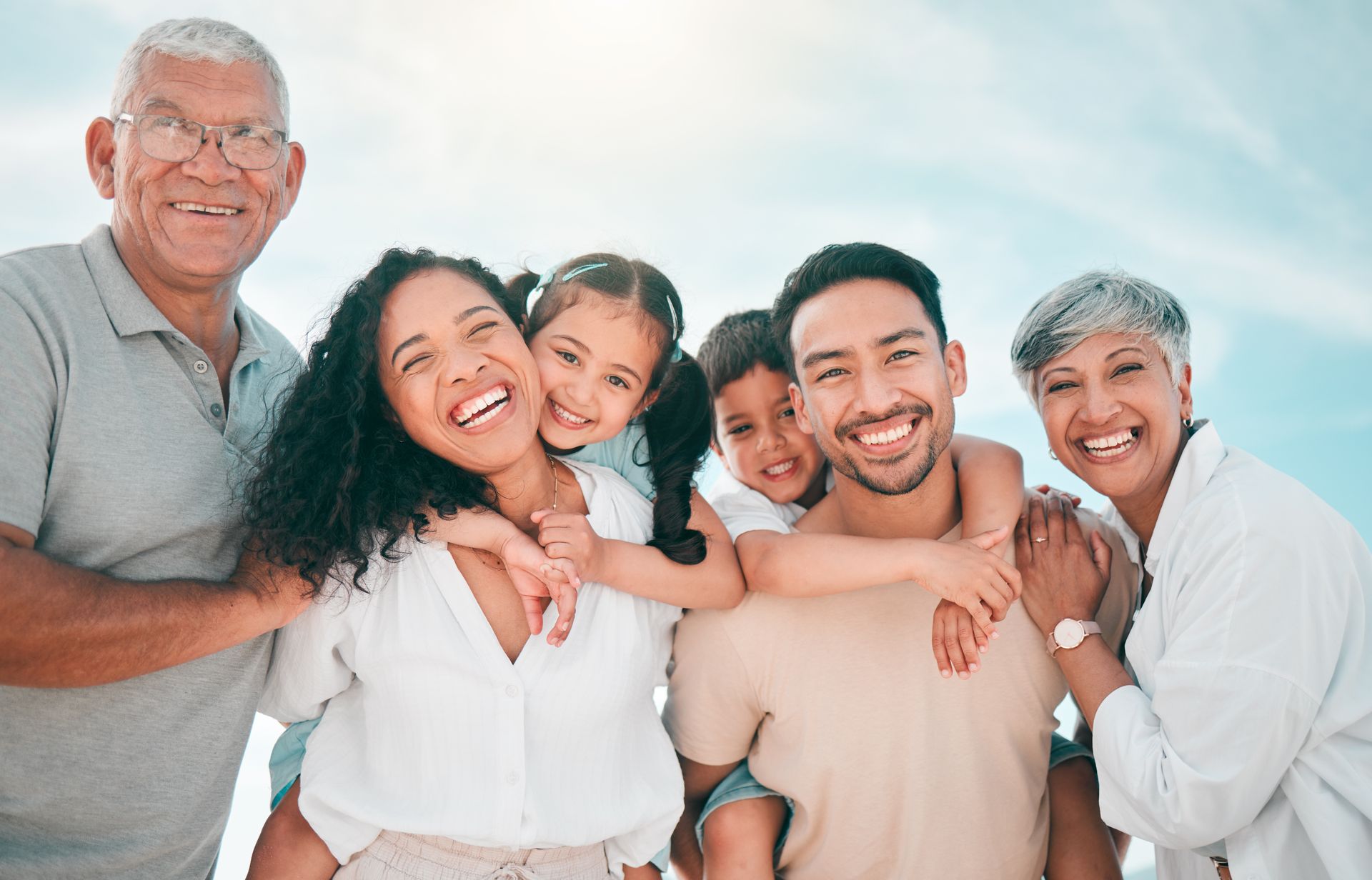 Multi-generational family smiling outdoors, with parents, grandparents, and children enjoying the sunshine.