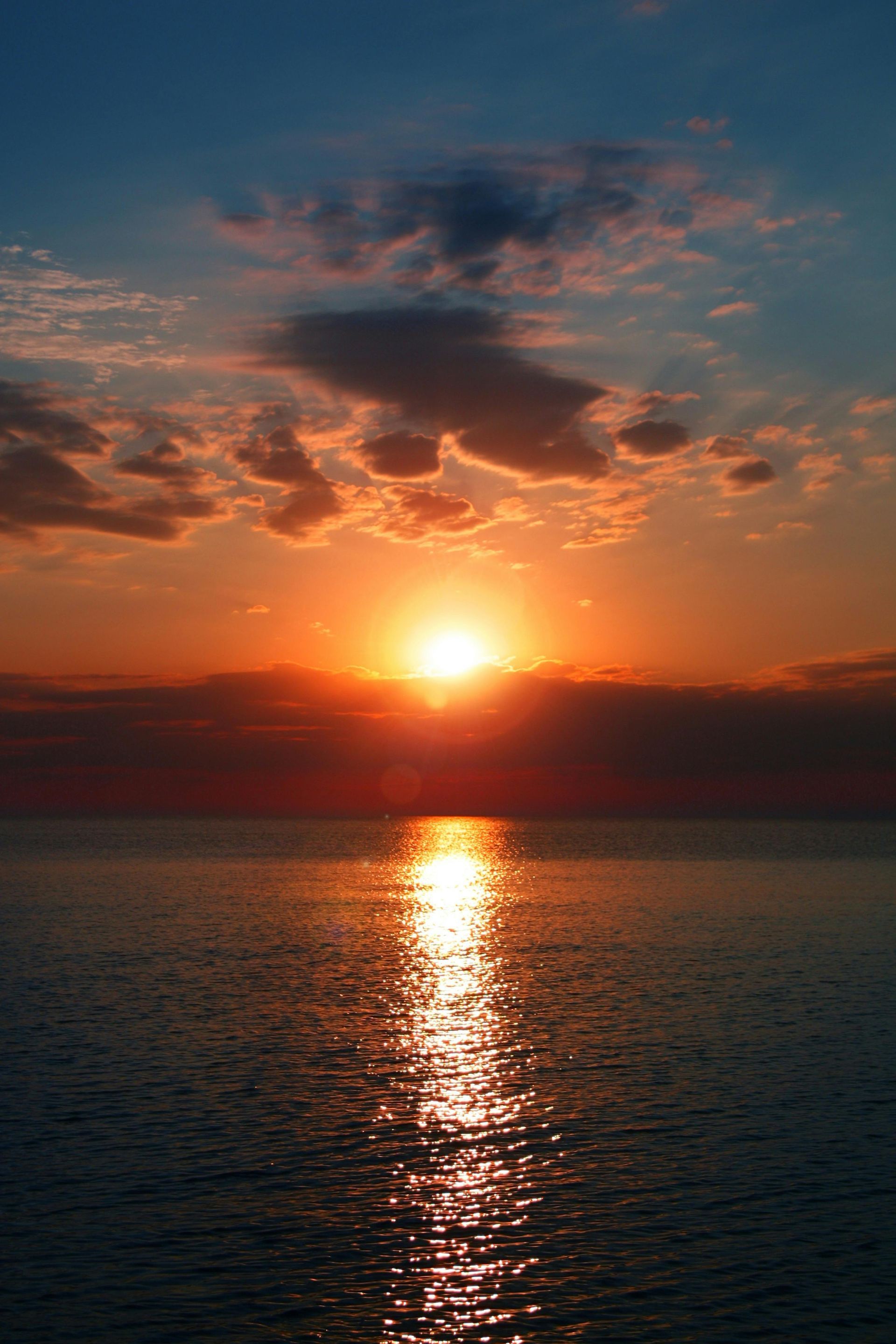 Sunset over calm water; sun reflects on the ocean. Orange and red hues illuminate the sky and sea.